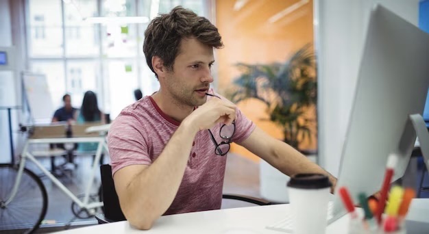 A man with glasses in his hands works at a computer in the office